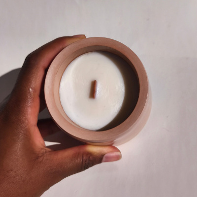 Vela branca numa jarra de cerâmica cor terracota numa mão sobre fundo branco