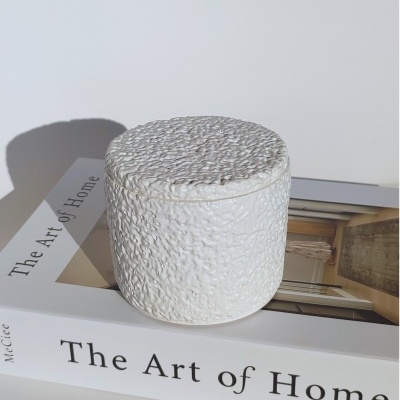 Pote branco texturizado sobre livro 'The Art of Home'