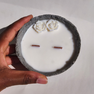 Vela branca com base cinzenta texturada e flores decorativas brancas