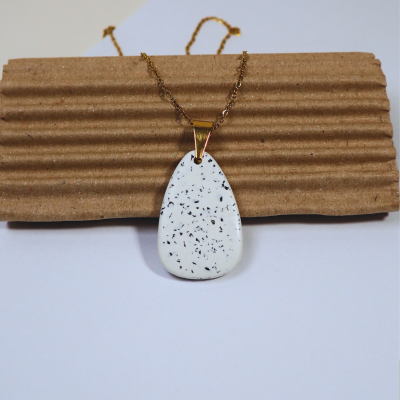 Colar com pendente gota branco manchado e corrente dourada sobre cartão castanho