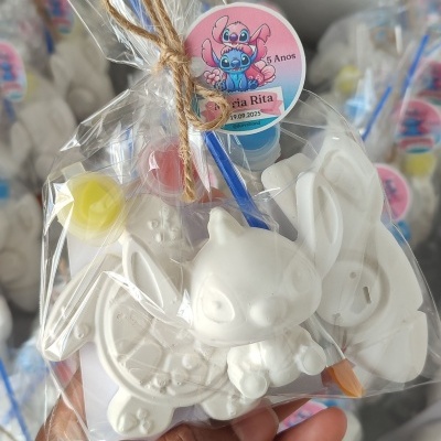 Kit de pintura com figura de cerâmica branca e tintas em saco transparente com etiqueta de aniversário.