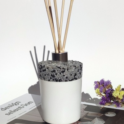 Difusor de aromas branco com topo cinza e varetas de madeira sobre livro e flores secas