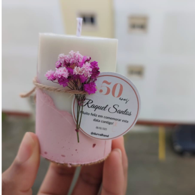 Vela decorativa branca e rosa com flores secas e etiqueta comemorativa