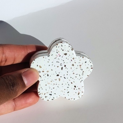 Objeto decorativo em forma de flor branco com pontos coloridos, segurado por uma mão.