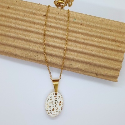 Colar dourado com pendente oval branco manchado dourado sobre cartão canelado