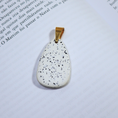 pendente branco com manchas pretas e argola dourada sobre livro aberto