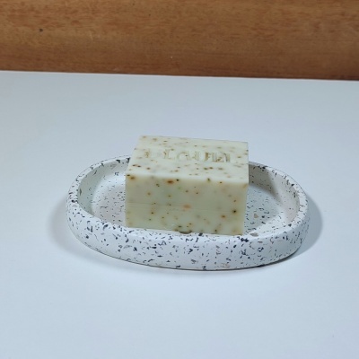 Sabonete bege com partículas escuras numa saboneteira branca com manchas pretas