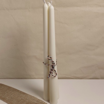 Três velas brancas amarradas com fio tricolor sobre superfície com faixa de tecido rústico