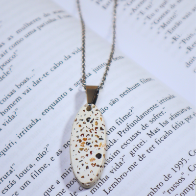 Colar com pendente oval branco com padrão castanho sobre livro aberto.