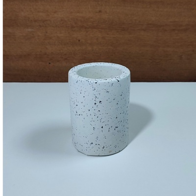 Copo cilíndrico branco com manchas pretas sobre mesa branca e fundo de madeira