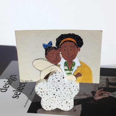 Postal ilustrado de mãe e filha sobre base cerâmica branca.