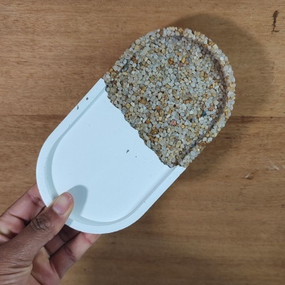 Recipiente branco com pequenas pedras coloridas segurado por uma mão sobre madeira clara