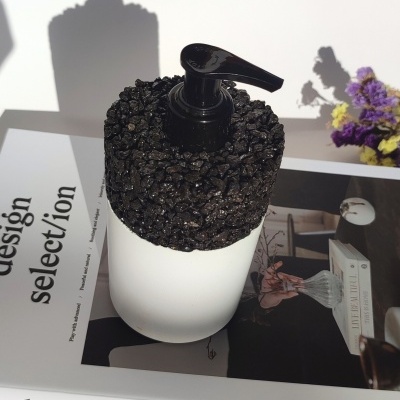Frasco branco com tampa preta texturizada sobre revista 'design selection' e flores ao lado