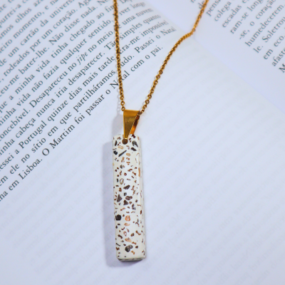 Colar com pendente branco manchado e cadeia dourada sobre livro aberto