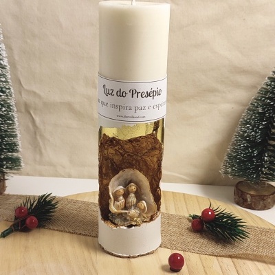 Vela branca com miniatura de presépio e rótulo, decorada com material dourado e decoração natalícia de fundo