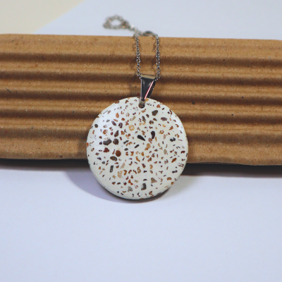 Colar com pendente redondo branco decorado em padrão de pedras em tons castanho e bege.