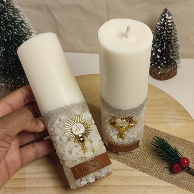 Duas velas brancas decoradas com pedras, ornamentos dourados IHS e etiqueta DRVM em couro