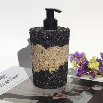 Dispenser para sabonete com decoração de pedras preto e castanho, sobre livros com flores ao lado.
