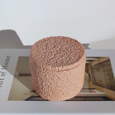 Caixa redonda de cerâmica cor de terracota com textura irregular sobre livro 'The Art of Home'.