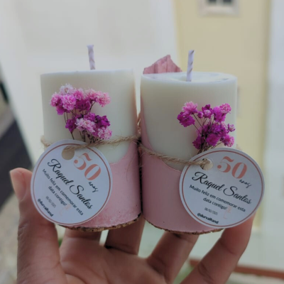 Dois conjuntos de velas brancas com base rosa e etiquetas comemorativas com flores roxas