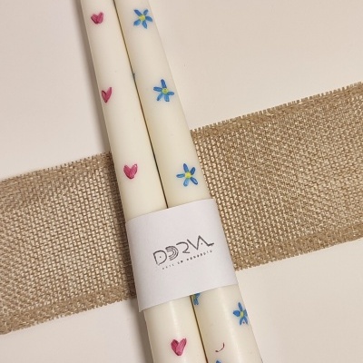 Velas brancas decoradas com corações e flores com rótulo DORVA sobre tecido rústico.