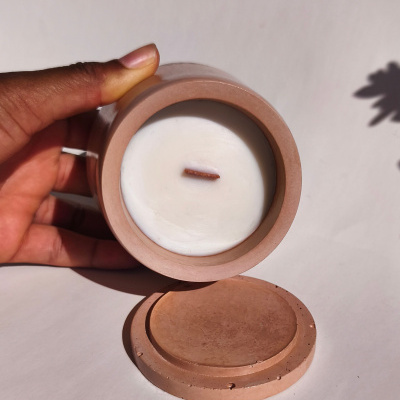 Vela branca em recipiente cerâmico castanho claro com tampa ao lado num fundo branco