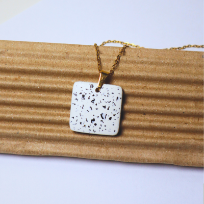 Colar dourado com pendente quadrado branco manchado em papel ondulado castanho