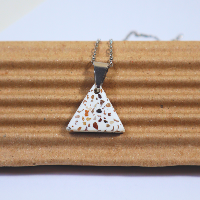 Colar com pendente triangular branco e manchas coloridas sobre fundo de cartão ondulado