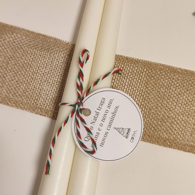 Duas velas brancas com etiqueta de Natal e fio tricolor