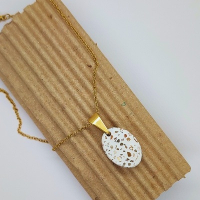 Colar dourado com pendente branco com manchas douradas sobre cartão ondulado