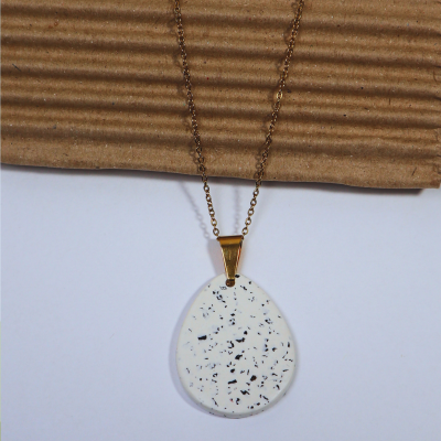 Colar dourado com pendente branco às manchas pretas sobre papelão ondulado castanho