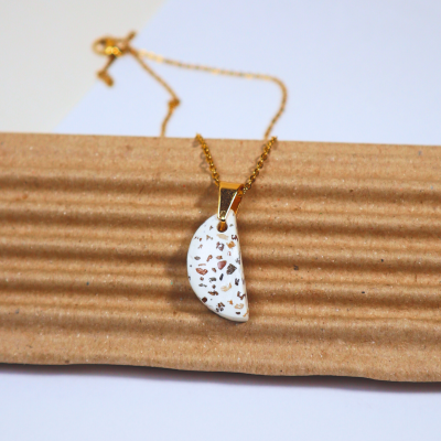 Colar dourado com pendente branco salpicado em cartão canelado castanho