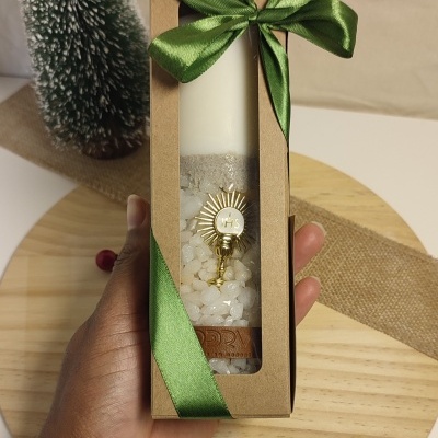 Vela branca decorativa com pedras brancas e adorno dourado numa caixa com fita verde.