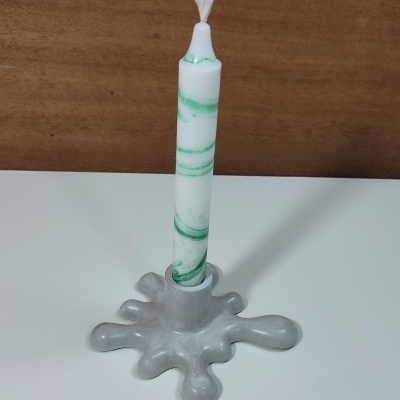 Castiçal cinzento com vela branca e verde sobre mesa branca com fundo de madeira