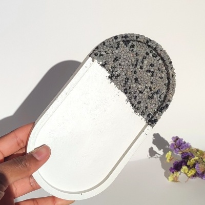 Bandeja pequena com textura de grãos e metade branca, segurada à mão, com flores ao fundo