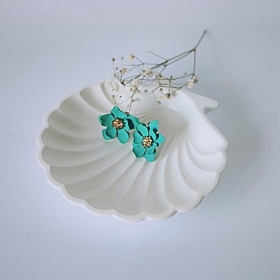 Brincos florais turquesa numa bandeja branca em forma de concha com raminho de flores secas