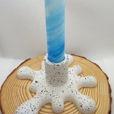 Castiçal branco com manchas coloridas e vela azul com padrão espiral sobre base redonda de madeira