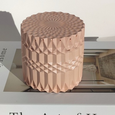 Recipiente decorativo rosa claro com padrão geométrico sobre livro 'The Art of Home'.