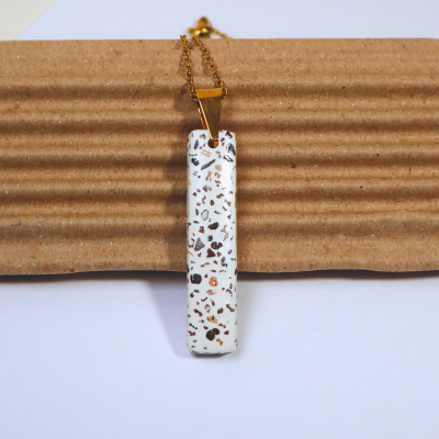 Colar com pendente retangular branco com manchas e corrente dourada sobre cartão corrugado castanho