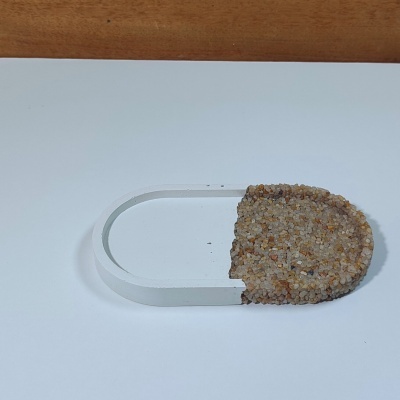 Objecto oval branco com metade coberta por pequenas pedras sobre superfície branca