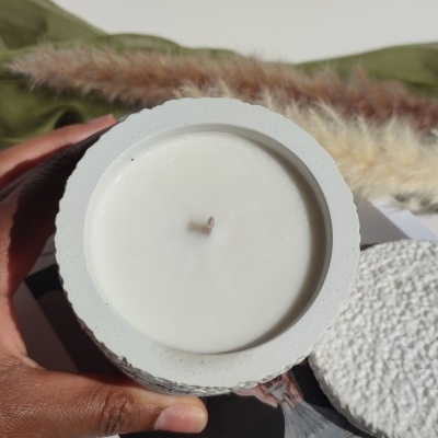 Vela branca em recipiente de cerâmica cinzenta texturada com tampa separada e fundo decorativo