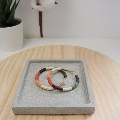Duas pulseiras coloridas de contas em bandeja cinza sobre mesa de madeira clara