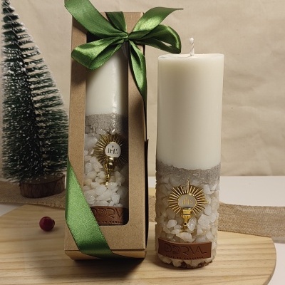 Candelabro religioso branco com base de pedras e emblema 'IHS' em caixa com fita verde.