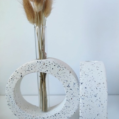 Peças decorativas em pedra branca com manchas pretas junto a vaso com flores secas