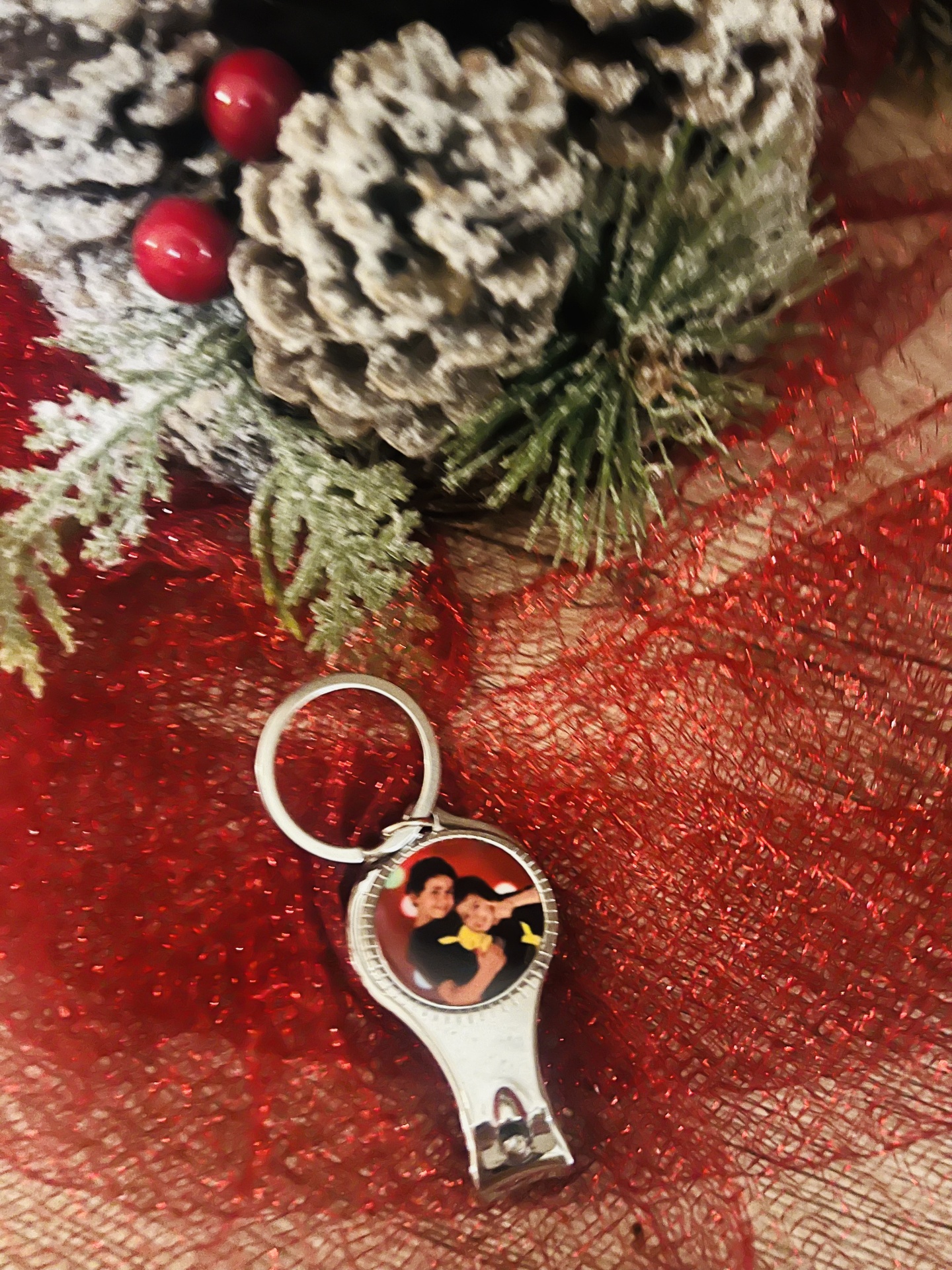 Chaveiro de metal com foto, sobre tecido vermelho, pinhas e ramos decorativos