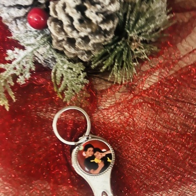 Chaveiro de metal com foto, sobre tecido vermelho, pinhas e ramos decorativos