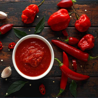 Molho de pimenta vermelha em tigela branca com pimentas vermelhas frescas e alho sobre madeira escura