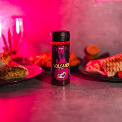 Garrafa de molho picante Volcano Sweet Chilli em mesa com wraps e luz rosa