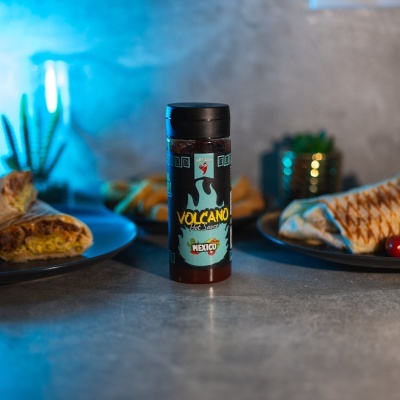Frasco de molho Volcano Hot Sauce no meio de pratos de wraps com plantas ao fundo
