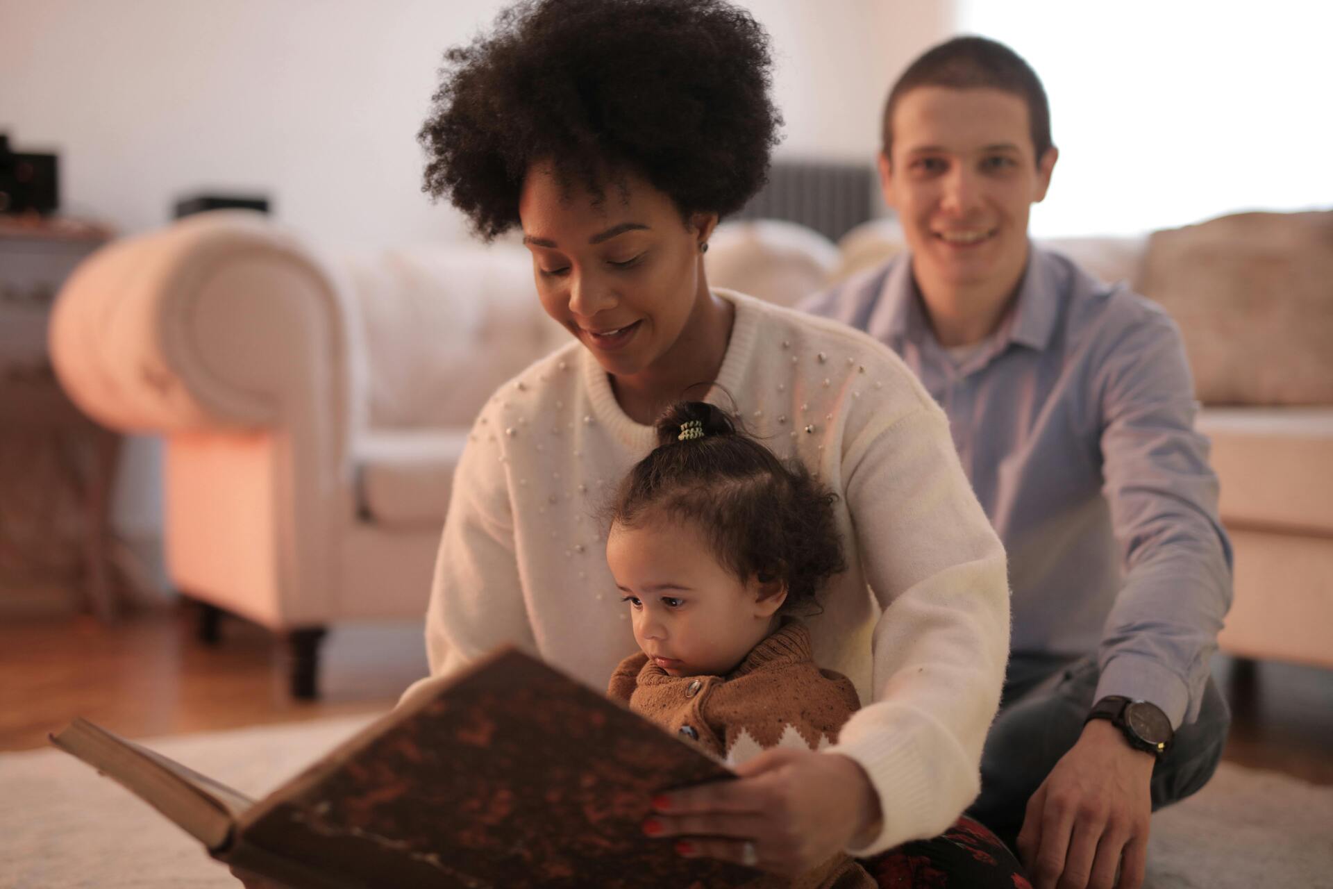Família lendo livro grande e aberto em sala com sofá bege ao fundo